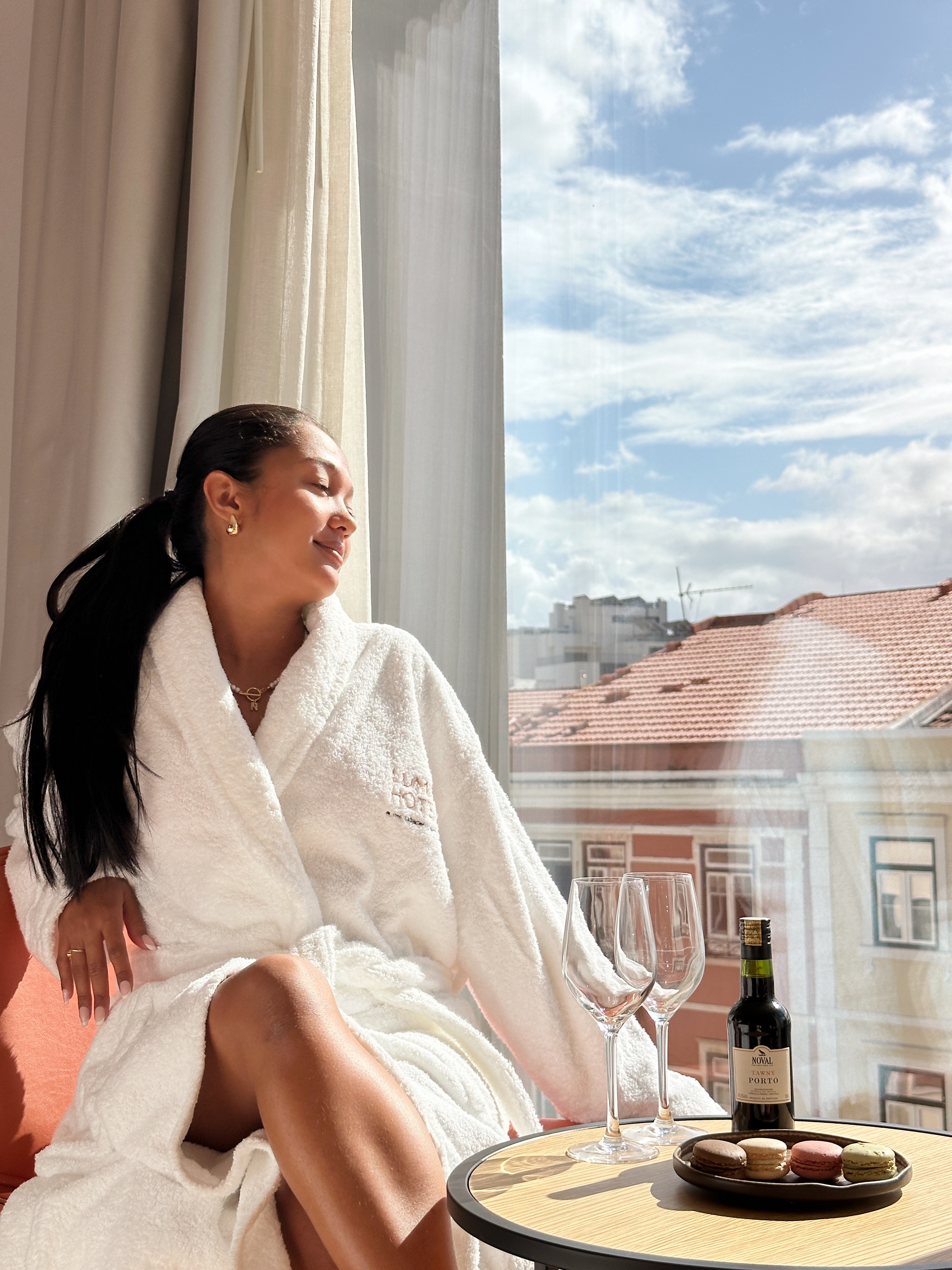 Nianch in a white hotel robe by a window with Porto rooftop views, wine glasses and macarons on the table